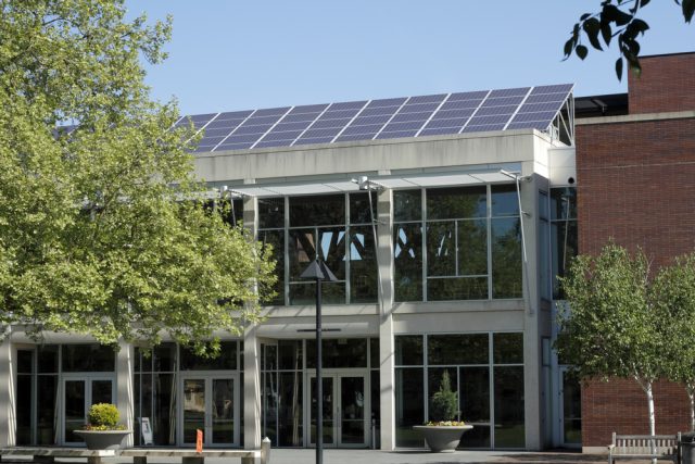 A large amount of solar panels line the front of a public library roof in a sunny spring day.